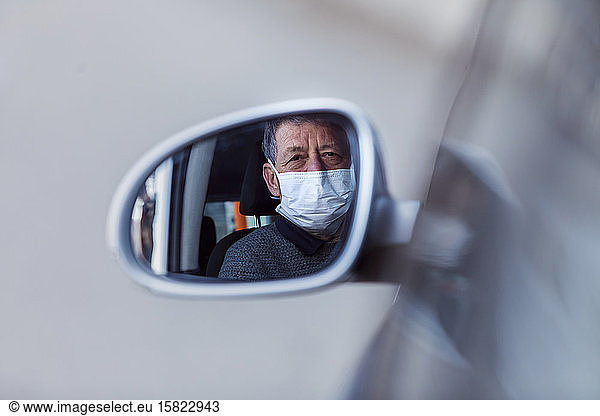 Reflection of senior man wearing mask in wing mirror of a car