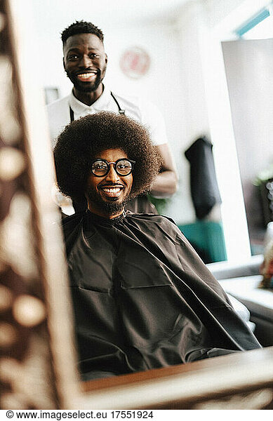 Reflection of smiling male hairdresser and customer in barber shop