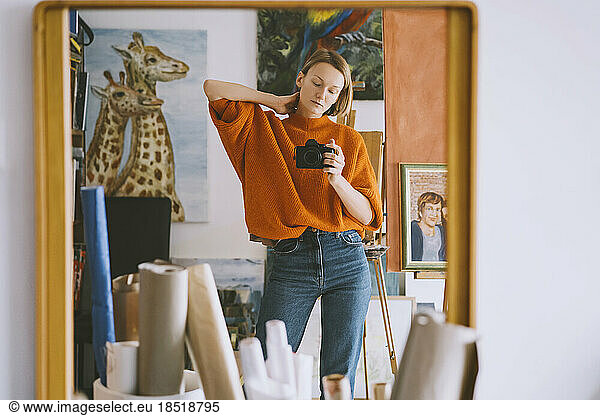 Reflection of woman holding camera on mirror at art studio