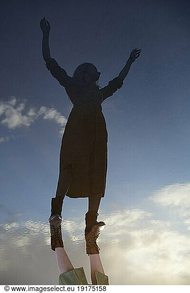 Reflection of woman with arms raised in water puddle