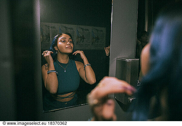 Reflection of young woman looking at mirror reflection in nightclub bathroom