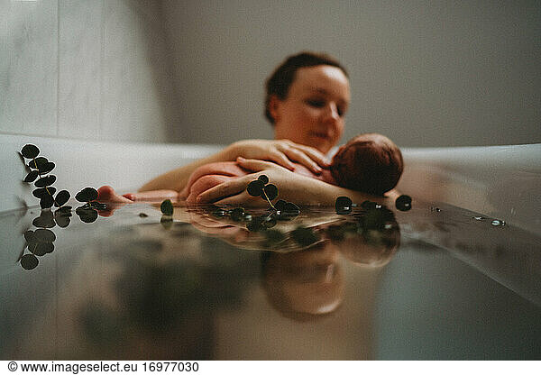 Reflection on water of mom breastfeeding newborn baby in bath tub