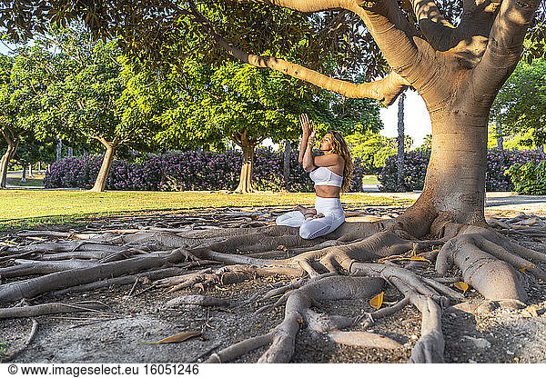 Reife Frau  die auf Wurzeln im Park sitzt und meditiert