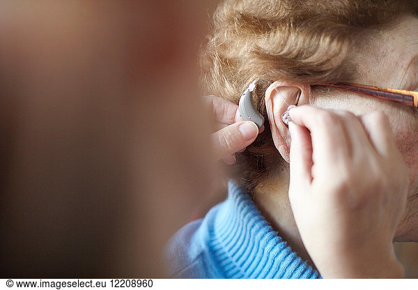 Reife Frau hilft älterer Frau beim Einsetzen des Hörgeräts  Nahaufnahme  differenzierter Fokus