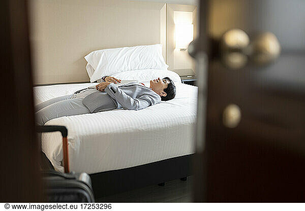 Reife Frau in Businesskleidung auf dem Bett einer Hotelsuite liegend