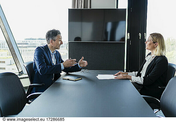 Reifer Geschäftsmann gestikuliert  während er mit einer weiblichen Mitarbeiterin im Sitzungssaal diskutiert