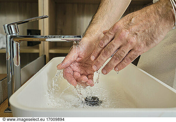 Reifer Mann beim Händewaschen unter fließendem Wasser im Badezimmer zu Hause