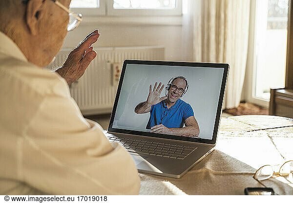 Reifer Mann grüßt älteren Mann per Videoanruf über Laptop zu Hause