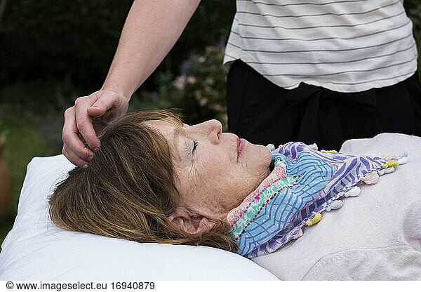 Reiki therapist with a client in a therapy session touching meridian points on the body.