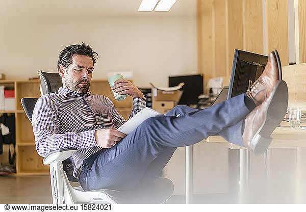 Relaxed businessman reading document at desk in office