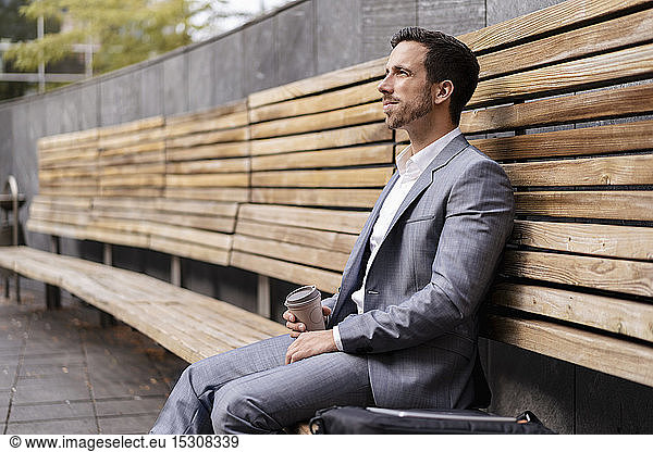 Relaxed businessman sitting on wooden bench in the city