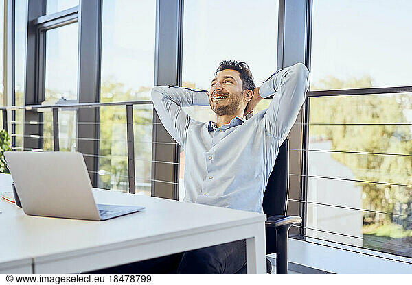 Relaxed businessman with hands behind head sitting on chair at office