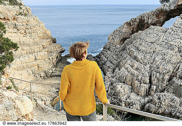 Relaxed elderly woman contemplating sea view with cliffs during sunset