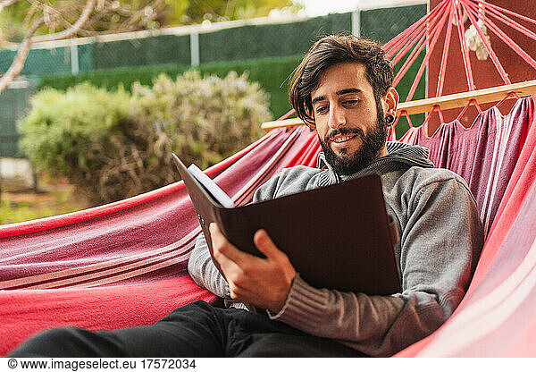 relaxed hipster man in hammock reading agenda