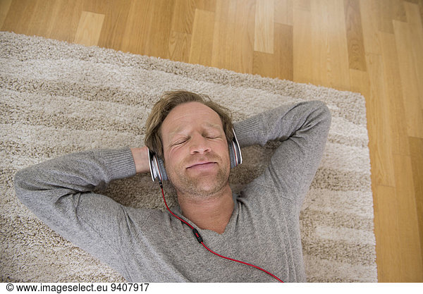 Relaxed man lying on rug listening to music
