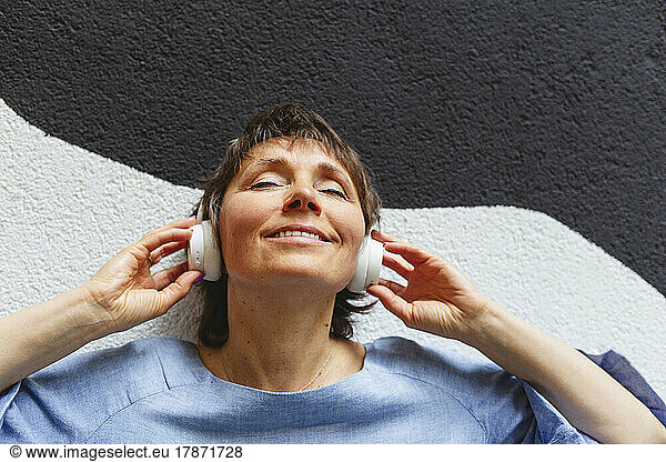 Relaxed mature woman listening music leaning on wall