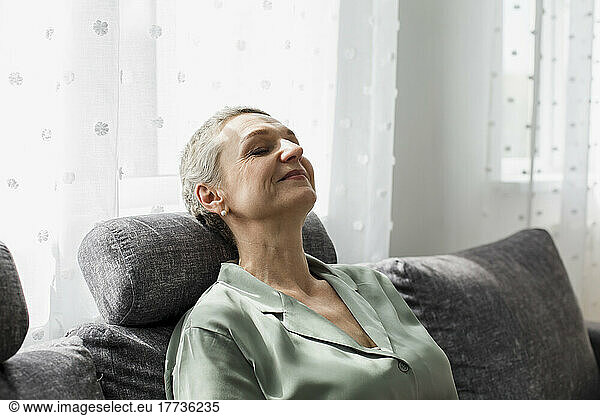 Relaxed mature woman on couch in living room with closed eyes