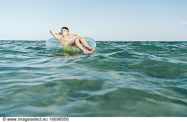 relaxed white boy swimming in a float in the sea enjoying calm waves in summertime