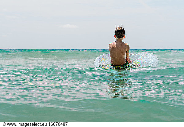 relaxed white boy swimming in a float in the sea enjoying calm waves in summertime. Backwards horizontal photo