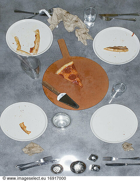 Remains of a pizza meal with leftover slice and crusts  glasses and plates and napkins.
