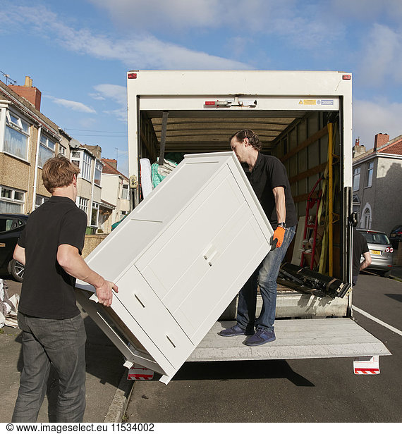 Removals business. Two men lifting a wardrobe onto the removals van.