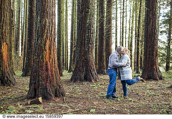 Retired couple kiss romantically in forest.