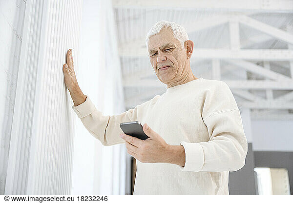 Retired man with smart phone touching radiator at home