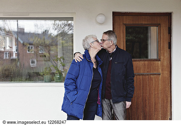 Retired senior couple kissing while standing against house