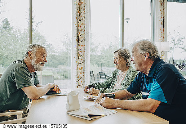 Retired senior friends talking while sitting at dining table in nursing home