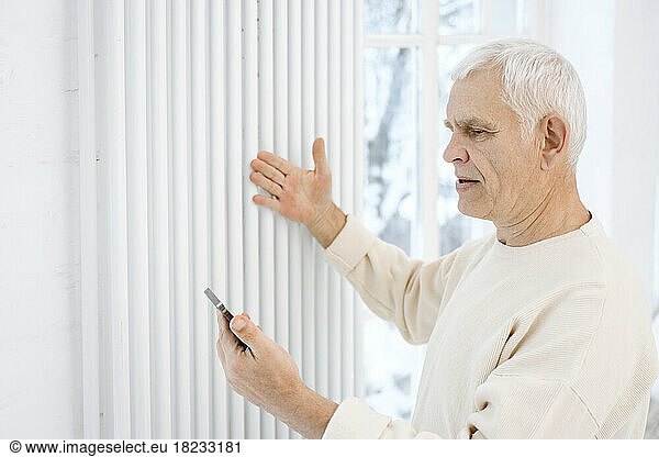 Retired senior man checking radiator holding smart phone at home