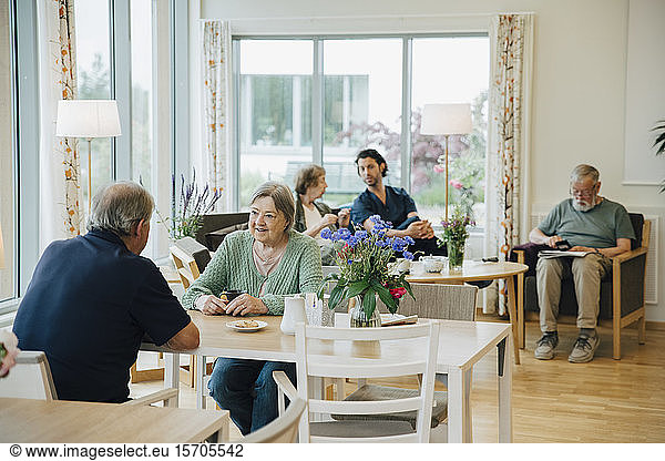 Retired senior men and women sitting with male nurse at elderly nursing home