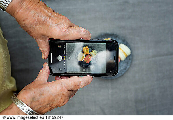 retired woman taking pictures on her phone of macarons