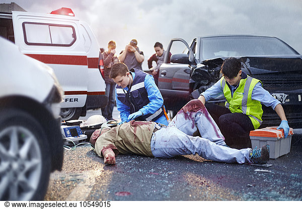 Rettungskräfte neigen zu blutigen Autounfallopfern auf der Straße