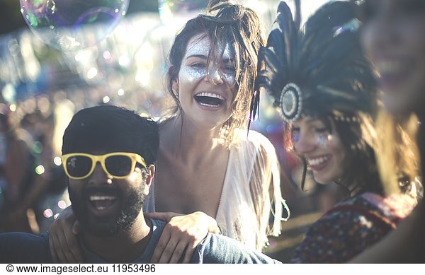 Revellers at a summer music festival young bearded man wearing yellow sunglasses and women with feather headdress and painted faces.
