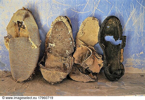 Rickety  decayed shoes leaning against blue wall  rotten shoes on the floor  rotten shoe  shoe wreck  rotten kicker  worn-out shoe  worn-out shoe
