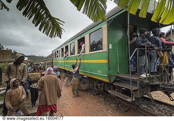 Riders look out windows and local vendors offer fruit for sale on the famous FCE railroad train in Madagascar.