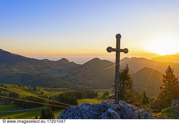 Rising sun illuminating Christian cross standing at summit of Sudelfeldkopf mountain