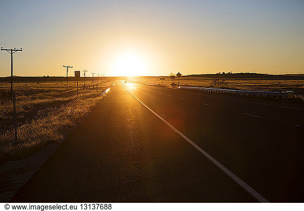 Road amidst field against clear sky during sunset
