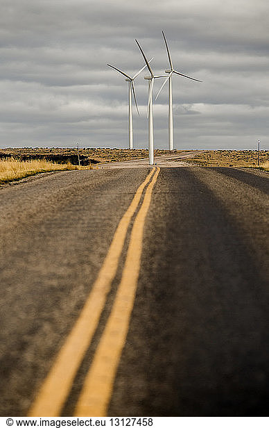 Road leading towards windmills against cloudy sky at farm