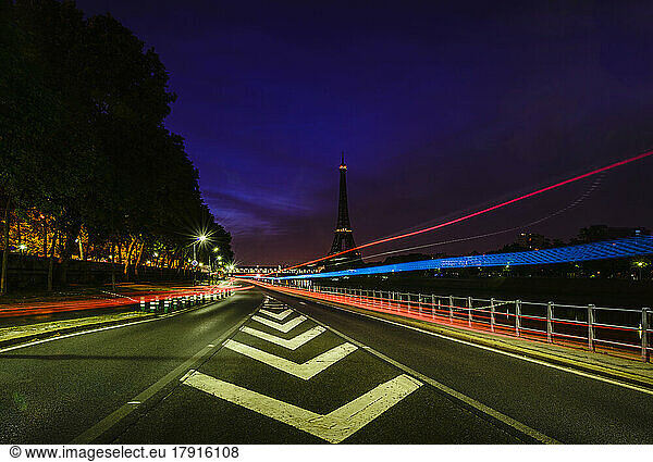 Road markings and coloured light trails at night on a straight road in Paris.