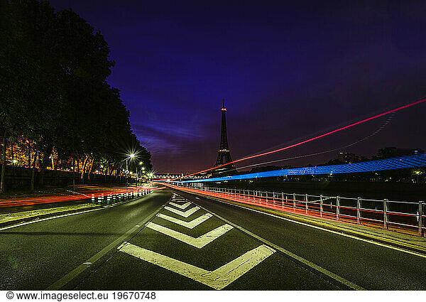 Road markings and coloured light trails at night on a straight road in Paris.