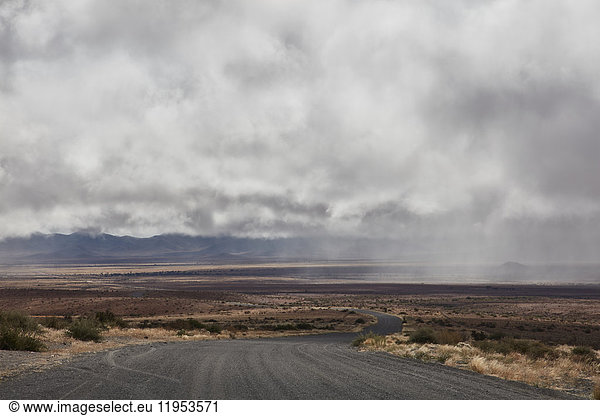 Road running through grassland under storm clouds.