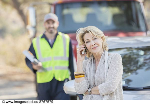 Roadside mechanic behind woman on cell phone