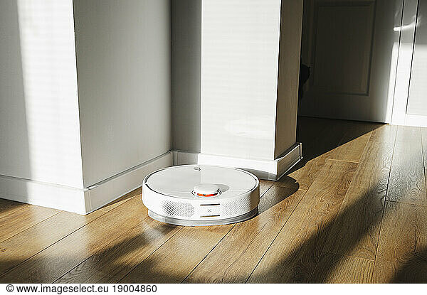 Robot vacuum cleaner on hardwood floor at sunny day