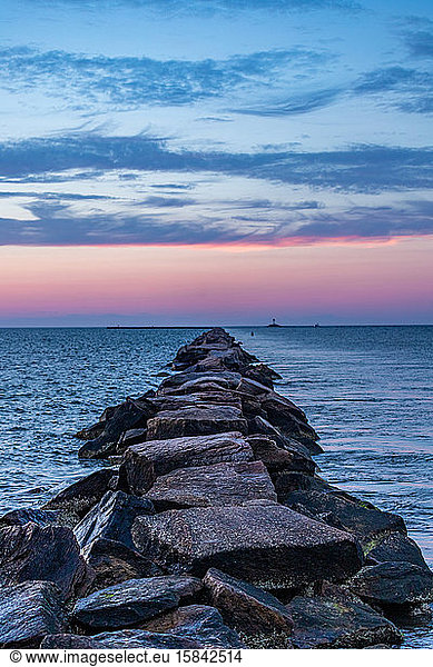Rock pier leading out into the ocean under a pink sunset sky.