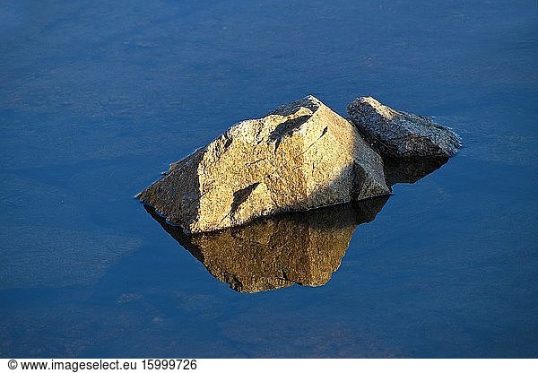 Rocks are reflected in the glassy water of a costal puddle.