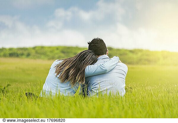 Romantic couple sitting on the grass hugging from the back  rear view of a couple in love hugging on the grass  A couple in love sitting on the grass hugging from the back
