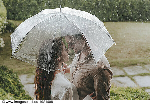Romantic couple standing with umbrella in rain at garden