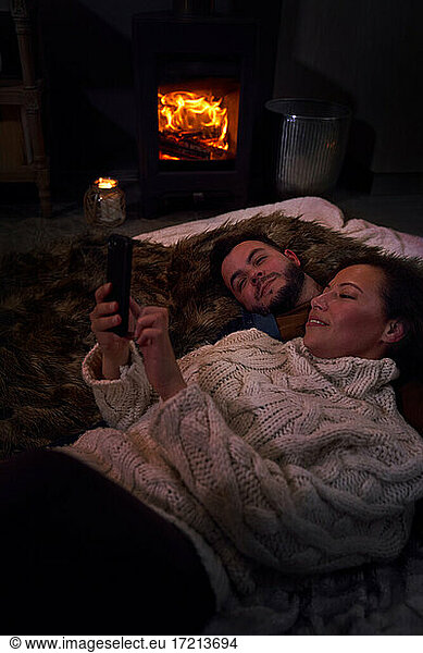 Romantic couple using smart phone at cozy fireside