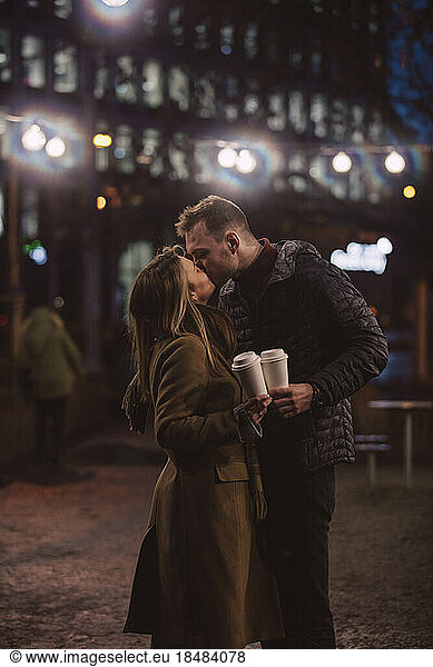 Romantic couple with disposable cups kissing each other at night